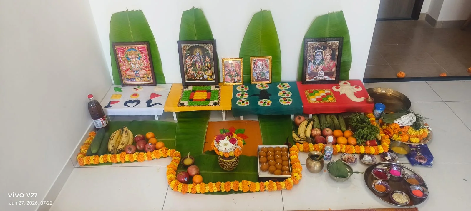 Home puja arrangement with deity frames, banana leaves, fruits and sweets
