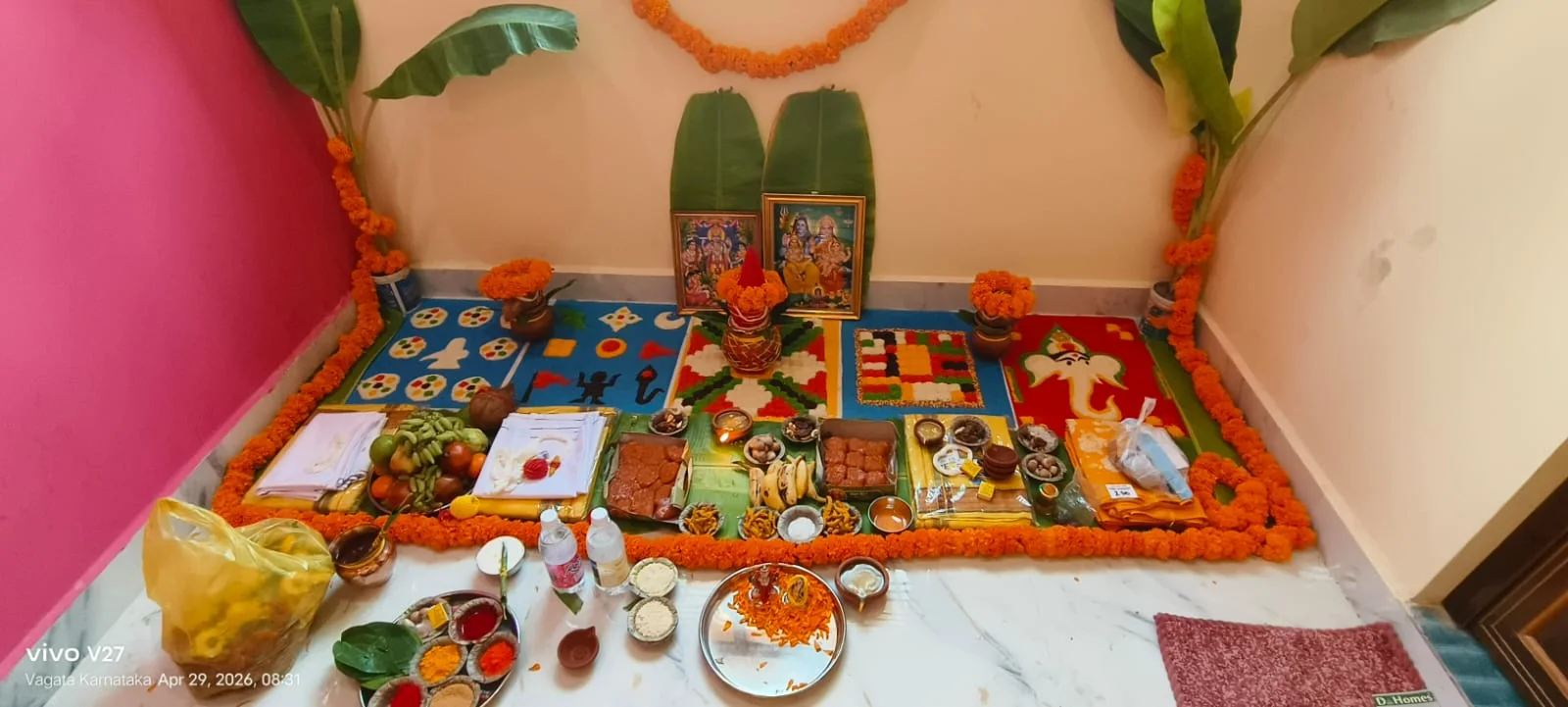 Home temple puja setup with deity frames, rangoli, fruits and ritual items