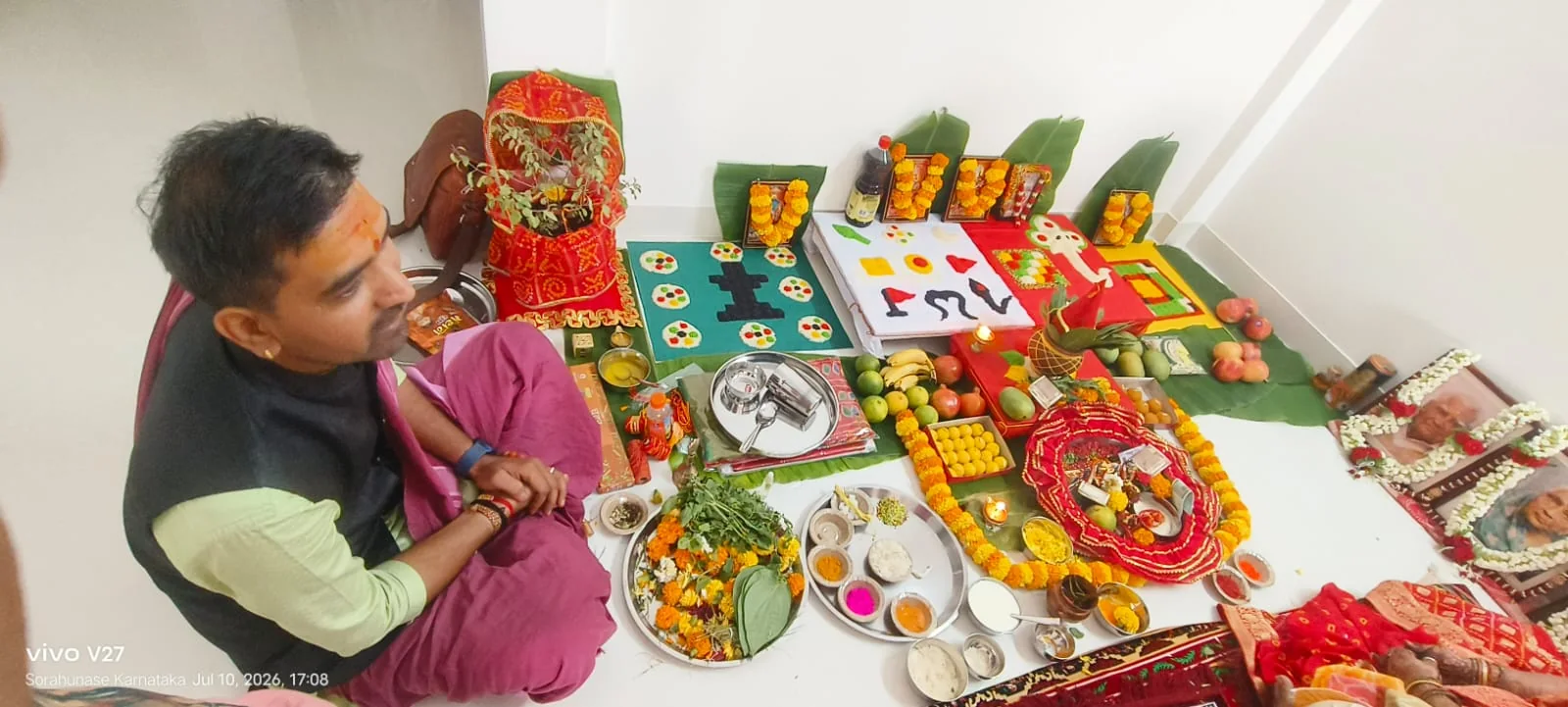 Pandit seated beside a prepared home puja setup with offerings
