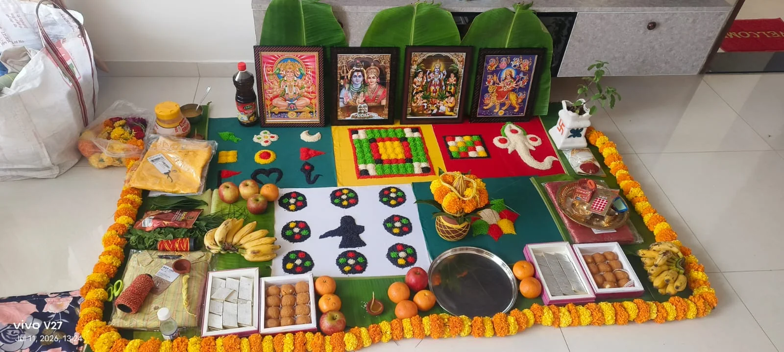 Puja arrangement with deity frames, banana leaves, sweets and fruits
