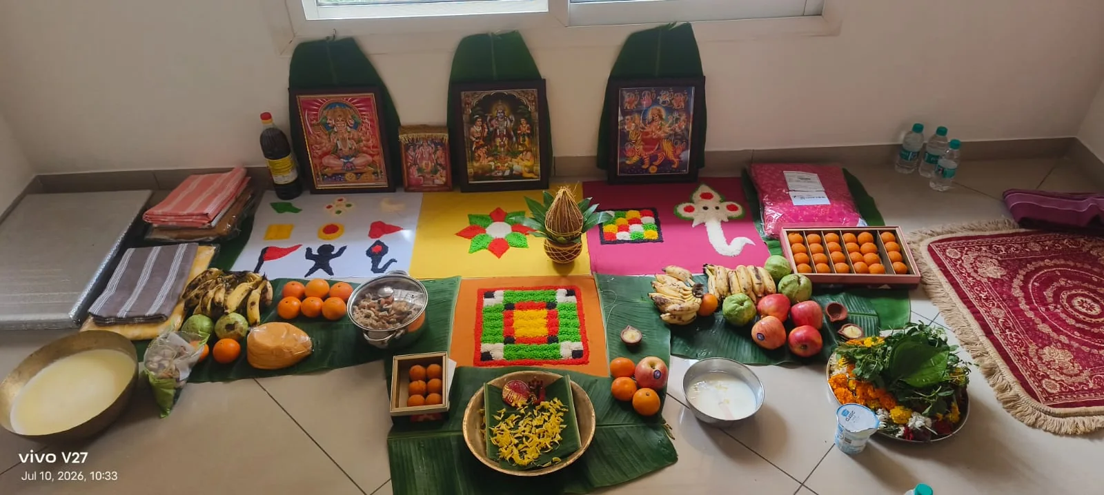 Home puja setup with rangoli, fruits, sweets and devotional pictures